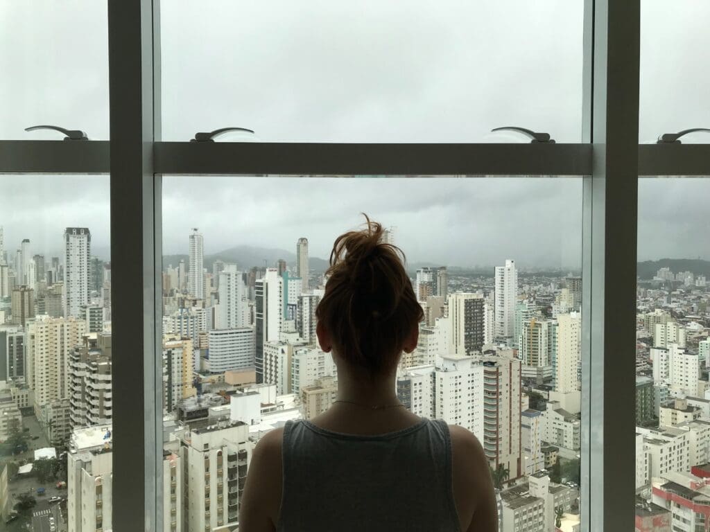 Rebrand • Worldly-Minded A woman stares out a window overlooking a city. The steps to quit alcohol include rebranding yourself and starting fresh after being done drinking