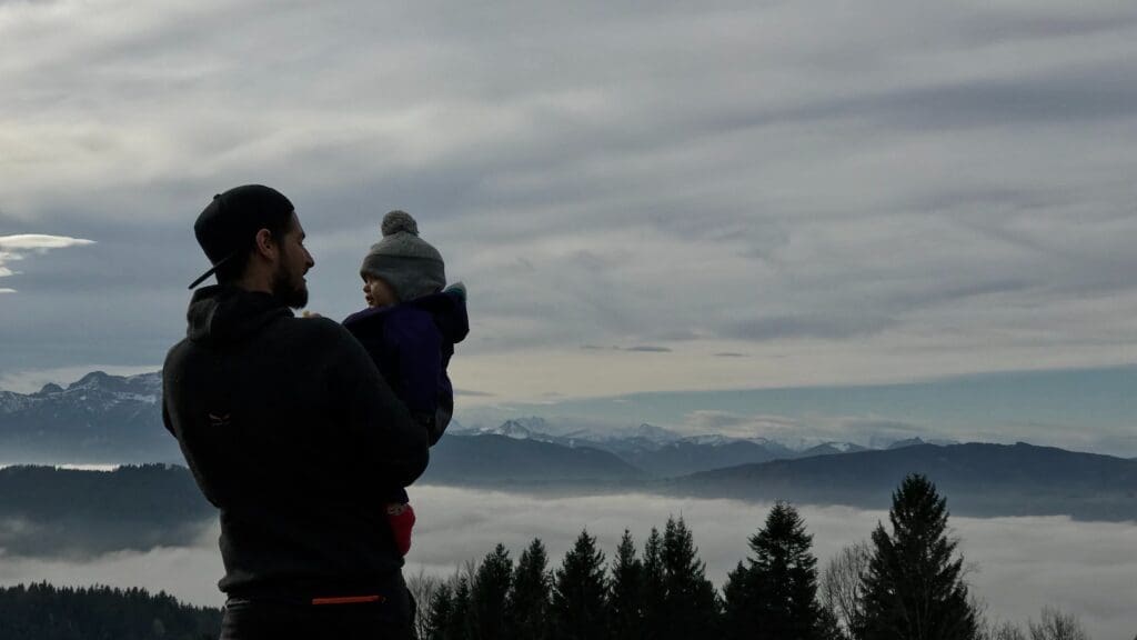 A man holds his baby overlooking a valley. Everything that we learn to do and say and think is programmed into us from infancy